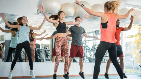 Ομάδα αθλητών που εκτελούν jumping jacks σε ομαδικό πρόγραμμα γυμναστηρίου – Ο πλήρης οδηγός για τις δυναμικές και στατικές διατάσεις στην προπόνησή σου από το Gymscouter.