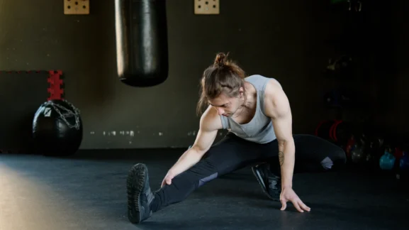 Αθλητής που εκτελεί δυναμικές διατάσεις σε γυμναστήριο για μυϊκή αποκατάσταση - Ο κρυφός σύμμαχος για τα αποτελέσματα που ονειρεύεσαι από το Gymscouter.